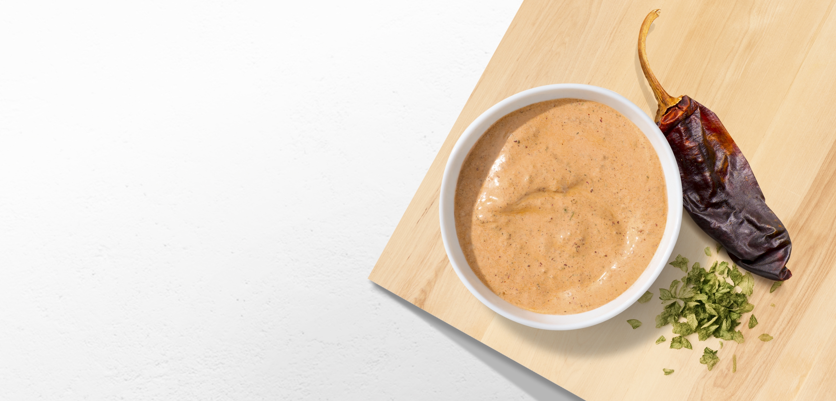 A side of Adobo Ranch on a cutting board around the fresh ingredients that go into it including Chipotle Chili pepper and fresh ranch herbs.